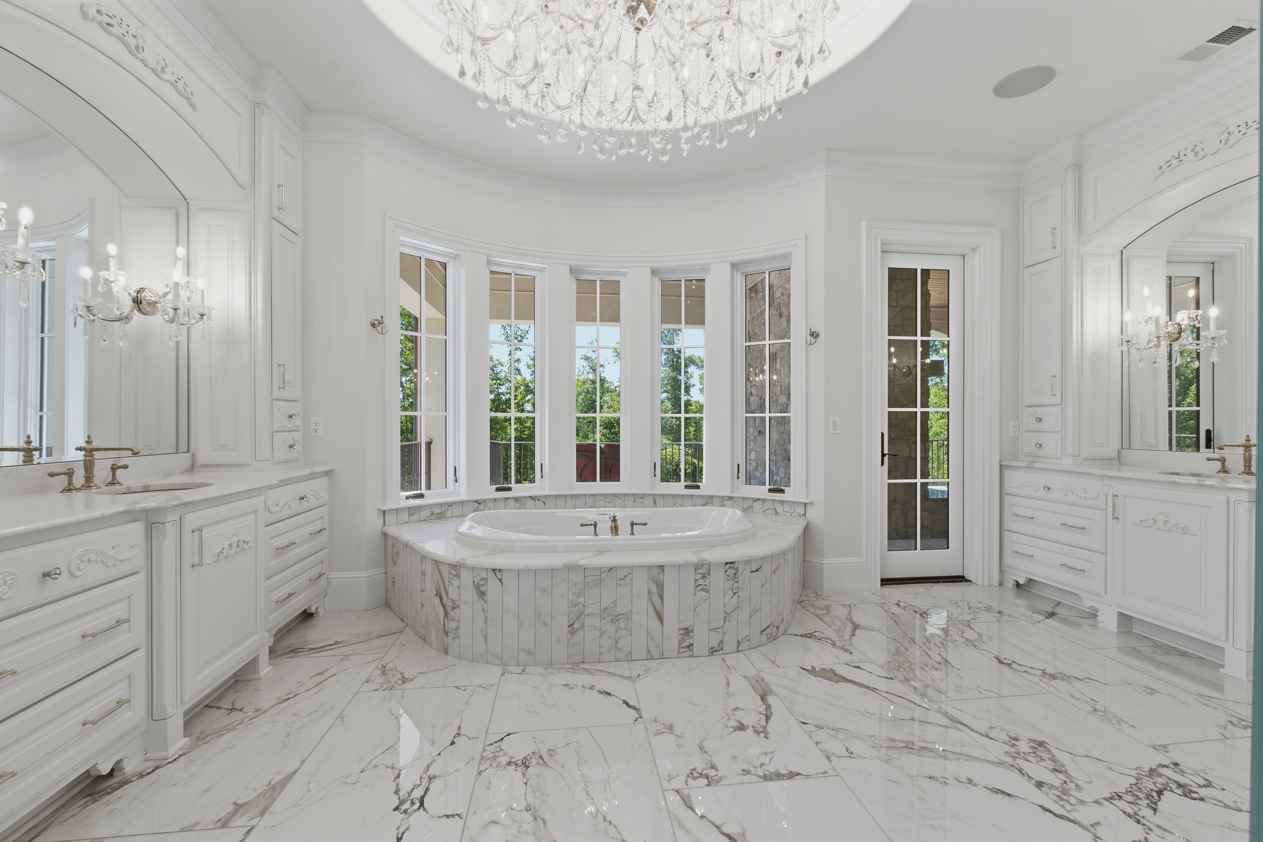 Primary bath with marble soaking tub set in a curved bay window overlooking the woods